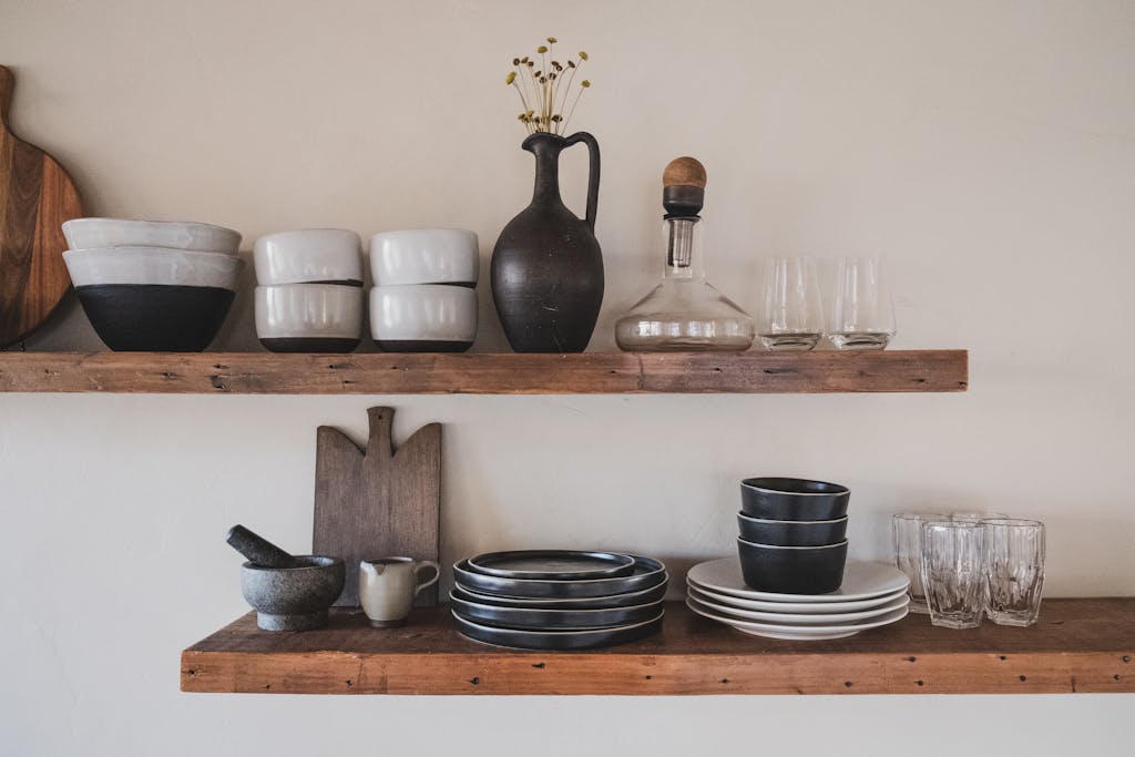 Stylish arrangement of ceramic bowls and glassware on rustic wooden shelves.