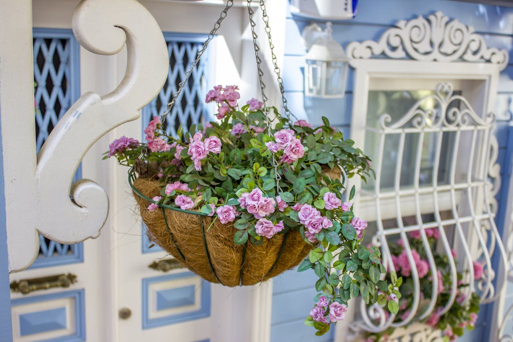 Beautiful pink flowers bloom in a hanging basket on a quaint small porch with intricate white designs.